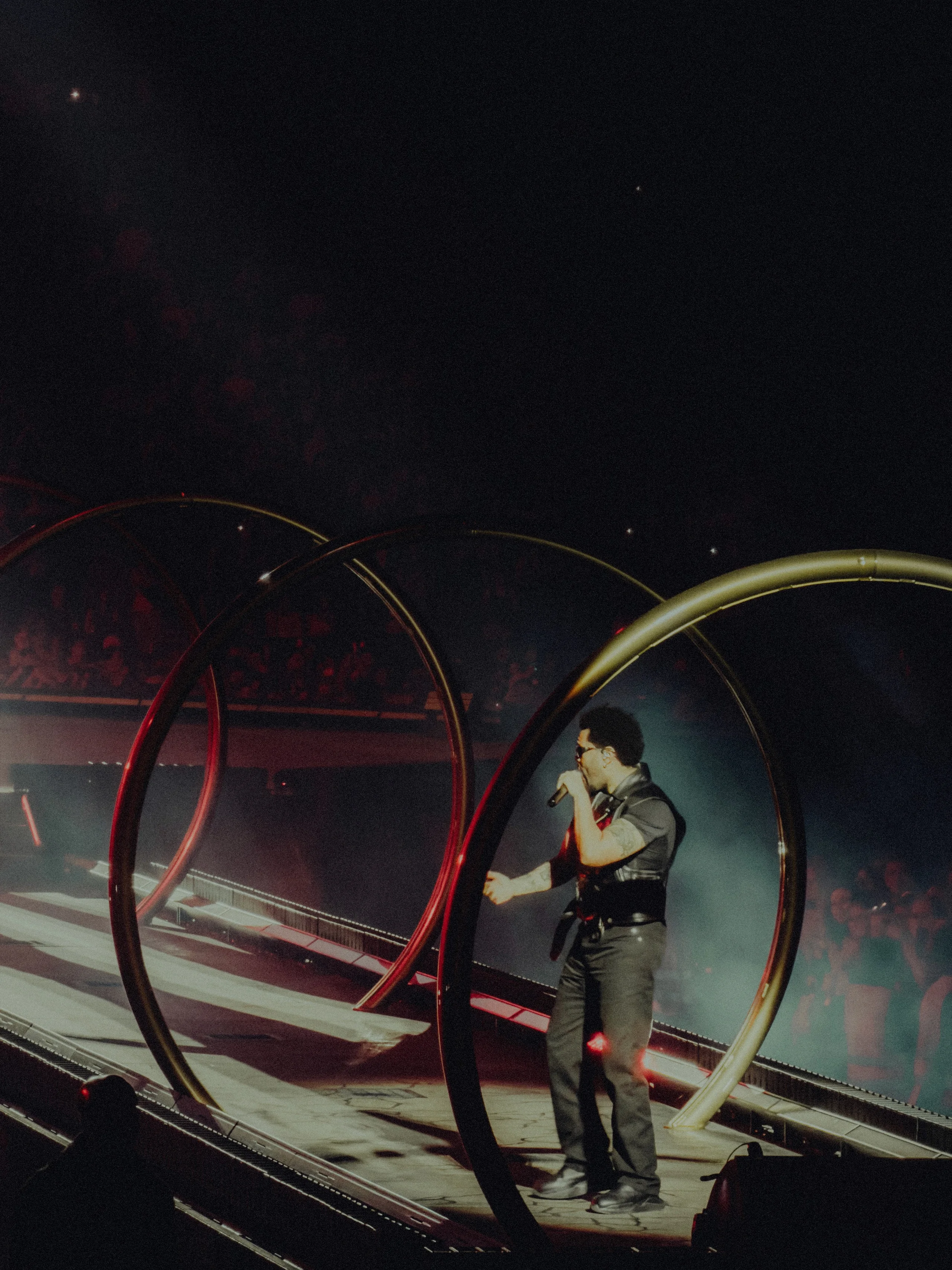 A performer on a dark stage framed by large metal rings